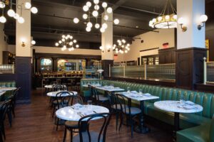 Photo of Avery Brasserie. There are small bistro tables, with green booths.
